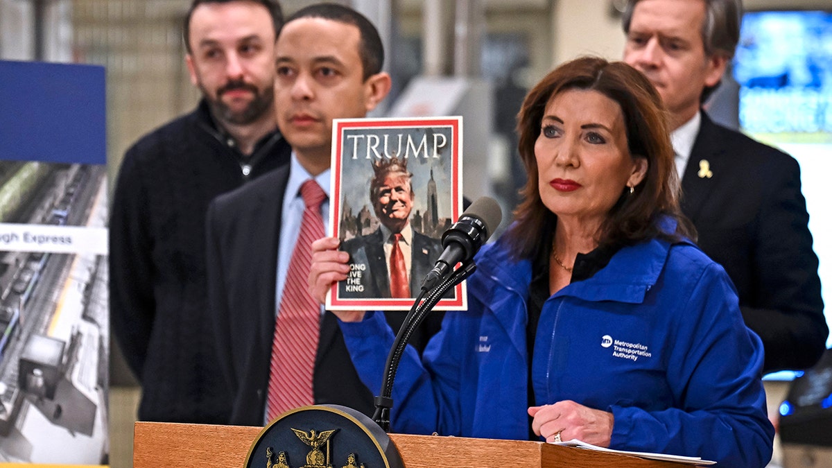 Kathy Hochul holding photo of Trump wearing a crown